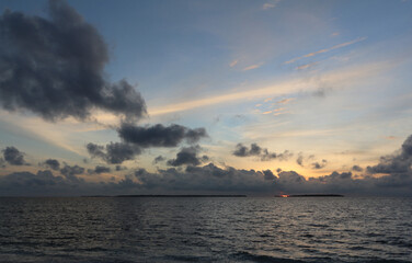 Sunset wiht blue sky and dark clouds in the ocean. Small Maldivian islands on the horizon.