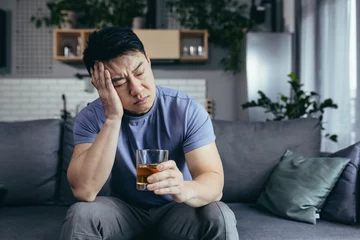 Poster Asian man at home alone, depressed drinking strong alcohol, single man © Liubomir