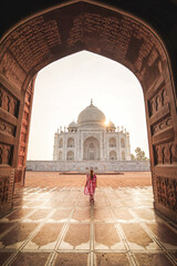 Woman wearing a red sari looking at the Taj Mahal at sunrise