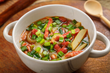 Bean soup with smoked meats and greens of Jewish cuisine cholit in a tureen and a wooden spoon.