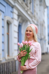 Fototapeta premium Girl holds bouquet of flowers and inhales their fragrance. Pretty girl takes lovely tulips with joy and smile. Portrait of surprised woman smelling flowers on the street.Girl holds bouquet of flowers