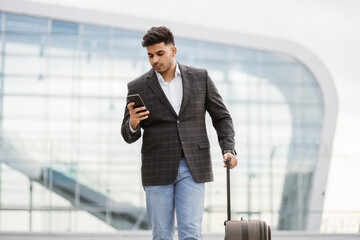Young Arabian man standing outside in front of airport gate and checking his flight schedule on...