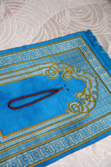 A blue, prayer rug, in the house, of a Muslim, his rosary, next to it, a prayer, rug, for worship in Islam,