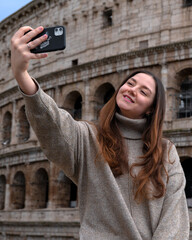 Tourist woman is taking a selfie with a smartphone in Rome with the Colosseum on the background	
