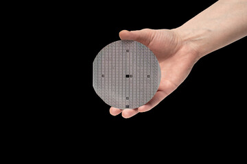 A hand holds a multilayer semiconductor silicon wafer with a microcircuit chip of a powerful Darlington transistor isolated on a black background - obrazy, fototapety, plakaty