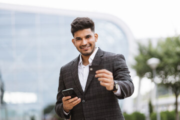 Online payment concept. Confident young Indian businessman in formal wear, stands outside at...