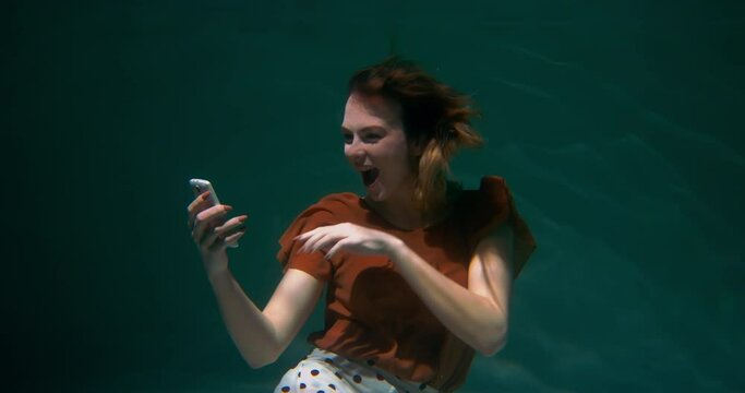 Amazing under water portrait of happy excited successful young woman reacting to great news on smart phone slow motion.