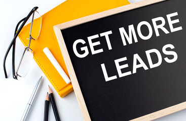 GET MORE LEADS text on the blackboard with notepad , pen, pencil