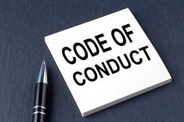 CODE OF CONDUCT text on the sticker with pen on the black background