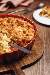 Mac and cheese. American Cheese pasta casserole with cheese sauce and crispy breadcrumbs in ceramic baking dish on wooden background. Selective focus
