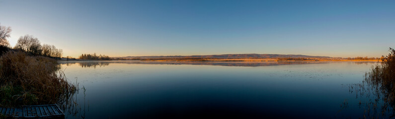 Panorama of autumn lake. Mirror reflection in water, blue sky.