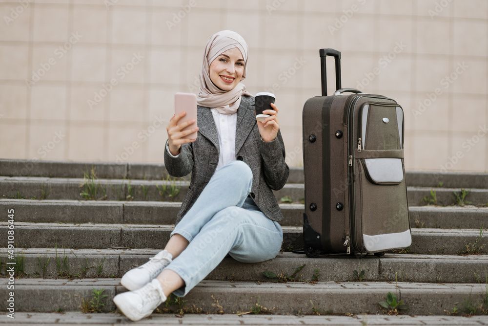 Wall mural focused young muslim businesslady in hijab sitting on stairs and working on wireless laptop, while w