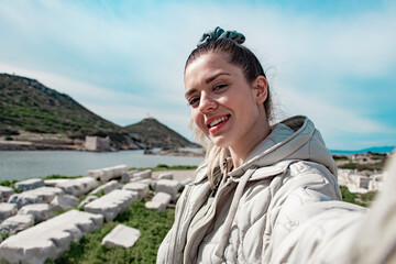 Happy beautiful woman takes a selfie portrait on vacation outdoor. She is in archaeological site. Travel alone concept.