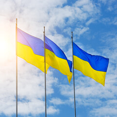 Banner with three Ukrainian flags on a background of blue sky and rising sun . High quality photo