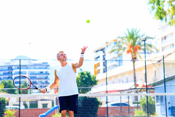 Senior caucasian man playing tennis on court holding tennis racket day light outdoors on fresh air