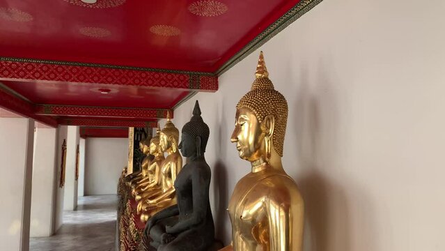 BANGKOK, THAILAND - Circa November, 2021: Golden buddha statues with bhumisparsa mudra gesture at Wat Pho, Temple of Reclining Buddha. Row of golden sitting buddha images on gilded pedestal