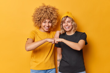 Cheerful two young women make fist bump agree to work as team dressed in casual outfit smile...