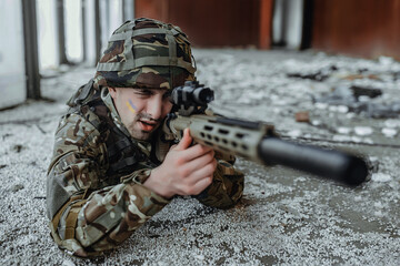 Military man sniper in a destroyed building lying aiming with a rifle, close up.