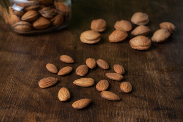 Almonds on a dark wooden table, next to some seeds.