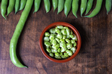 Fresh broad beans next to a clay plate with its fruit