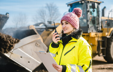 Woman with walkie talky on compost plant and wheel loader in background dispatching deliveries