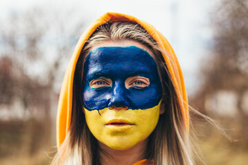 Outdoor portrait of young girl with blue and yellow ukrainian flag on her cheek
