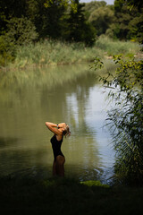 Beautiful slim woman in black swimsuit have a bath in a lake surrounded by wild vegetation.