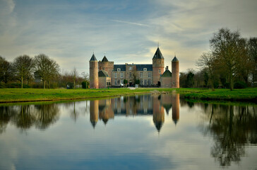 Fototapeta na wymiar Ein Schloss spiegelt sich im Wasser eines kleinen See in einer Parklandschaft