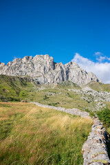 Fototapeta na wymiar green meadows with grass at the foot of a rocky mountain on a sunny summer day, a stone wall out of focus in the foreground, Formigal, Huesca, Spain