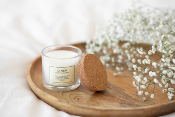White scented candle and a branch of gypsophila flowers on a wooden tray.