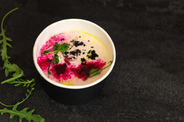 Cauliflower puree potato soup with arugula in round bowl on a black background, top view. Vegetarian healthy food delivery concept