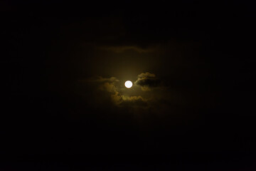 Full moon in the sky in total darkness, around a few clouds.
