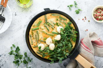Omelet with spinach, green beans, potato and spinach healthy food in black frying pan on grey stone old rustic background. Traditional frittata for breakfast Eggs tortilla Top view flat lay Copy space