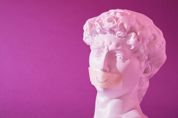 copy of the head of an antique statue of David with a taped mouth in pink neon light on a purple...