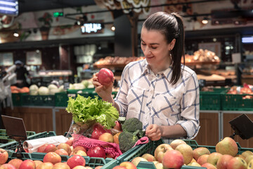 A young woman chooses fruits and vegetables in a supermarket.