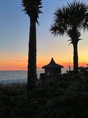 Palm trees and tiki hut silhouettes with sunset sky background on the beach