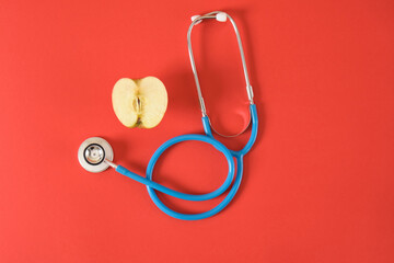an apple and a medical stethoscope on a bright red background