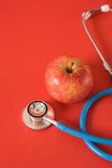 an apple and a medical stethoscope on a bright red background