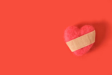 a heart made of natural wool with a glued adhesive plaster on a rich red background