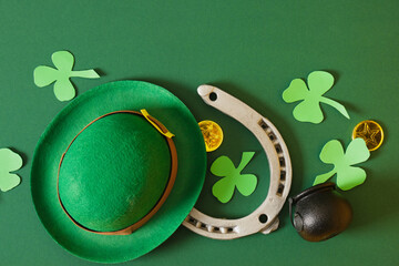 horseshoe, leprechaun hat, coins, cauldron and clover leaves from foamiran on a green background,...