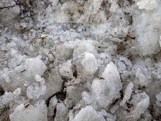 Lumps of melted snow on a spring day. The surface of dirty snow in the rays of the sun, top view. Snow and mud in the sun, close-up.