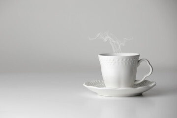 White cup and saucer of tea or coffee with steam on white background. Ceramic cup or mug with hot drink. Mock-up classic porcelain utensils. copy space