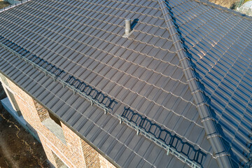 Obraz premium Closeup snow guard for safety in winter on house roof top covered with ceramic shingles. Tiled covering of building