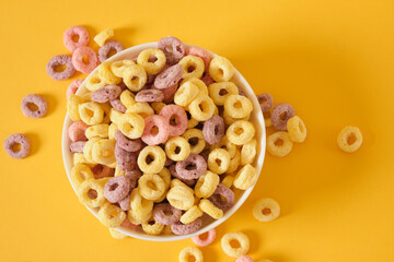 colored breakfast cereals laid out in a bowl on a yellow background top view, children's healthy...