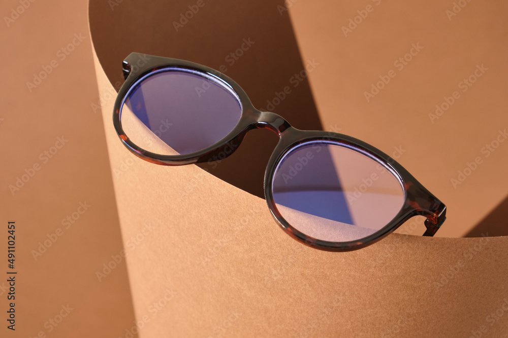 Wall mural beautiful stylish trendy modern eye glasses on rolled up paper, brown background