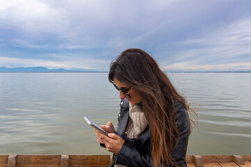 chica caucásica con pelo largo de color castaño y gafas de sol , trabajando con el teléfono móvil durante un paseo en barca por la albufera de valencia .