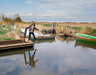 mujer haciendo equilibrios en embarcadero del puerto de sollana , en el parque natural de la albufera ,con barcas y cielo nublado .