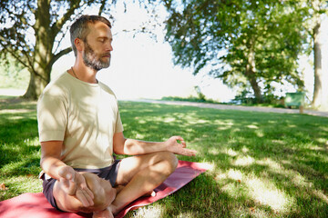 Serene underneath the trees. Shot of a handsome mature man meditating in the lotus position outdoors.