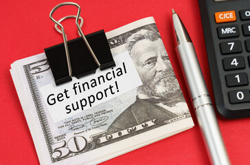 On a red surface lies a calculator, a pen, dollars and paper with the inscription - Get financial support