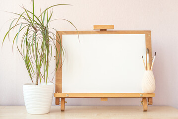 Blank white paper for painting mockup on a wooden easel and paln plant in pot on table at home...